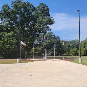 gray concrete plynth in circle with five flagpoles and trees in background