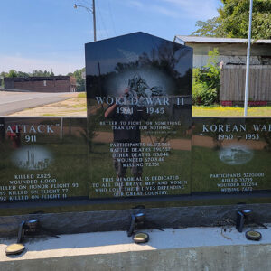 Black marble veterans memorial with headings "Attack 911" and "World War II" and "Korean War" and reflection of photographer on central portion
