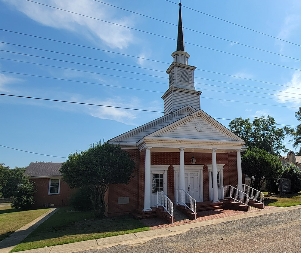 Multistory red brick and white wood church building with white columns in front and steeple