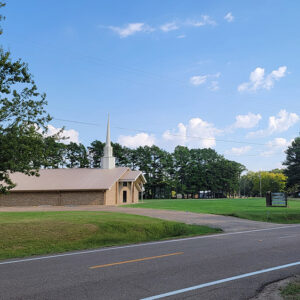 Single story blond brick church building with white steeple
