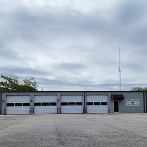 Single story gray metal fire department building with four garage doors