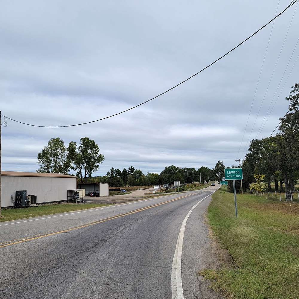 Rural highway with trees and single story building and sign reading "Lavaca"