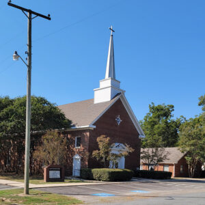 Multistory red brick church building with white steeple with cross on top and parking lot