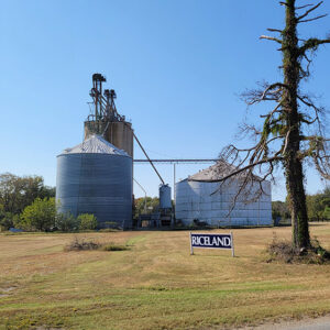 Two cylindrical silver and white metal buildings with taller silo behind and sign saying "Riceland"