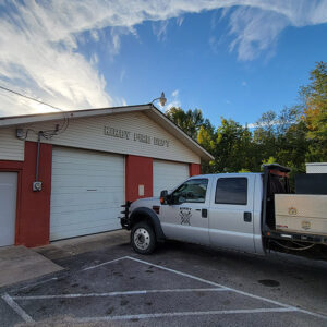 Single story red concrete block building with two bay doors and a truck parked in front