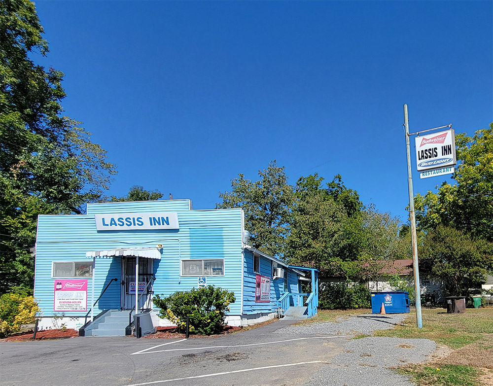 Single story blue wooden building with parking lot and trees
