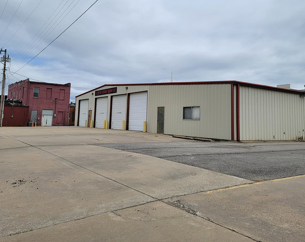 Single story beige metal building with four white bay doors and large paved lot
