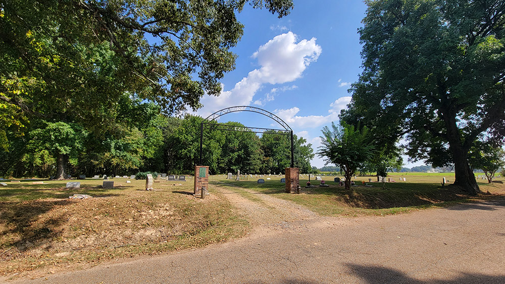 cemetery with graves and trees and an arched entrance