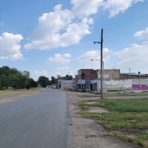 Small town street scene with many abandoned storefront buildings and trees in distance