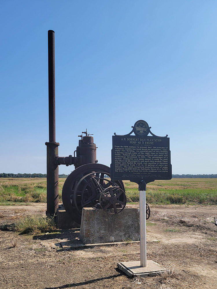 Rusted machinery on a concrete block and a historical sign in the middle of a field