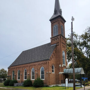Multistory brown brick church building with covered entrance and tall gray steeple