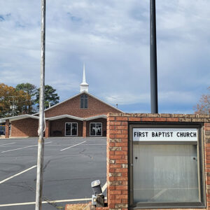 Red brick church building with steeple and large parking lot