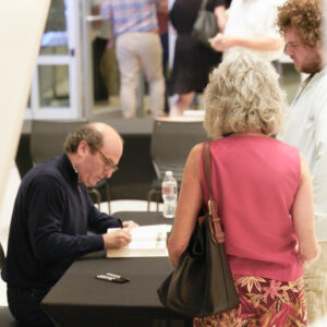 White man sitting at table signing books for people lined up