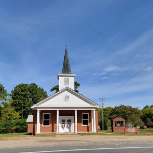 Single story red brick church building with covered entrance and steeple