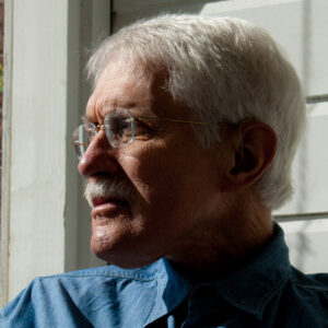side view of a white man with white hair and glasses staring into the distance