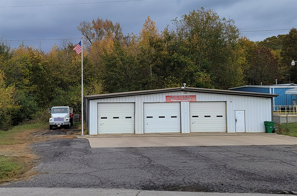 Single story white metal building with three garage doors and a truck parked beside