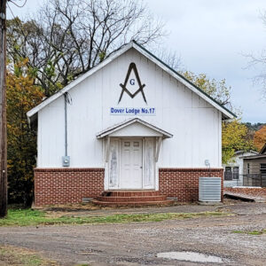 Single story orange brick and white wooden building with Masonic symbol