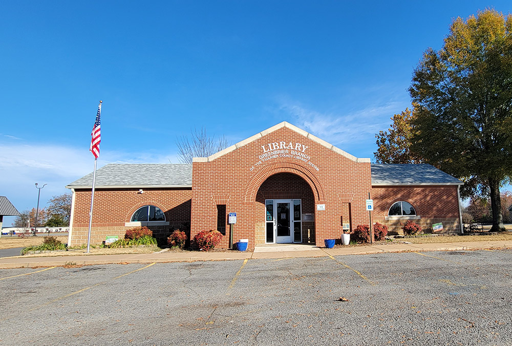 Single story red brick library building with covered entrance and parking lot