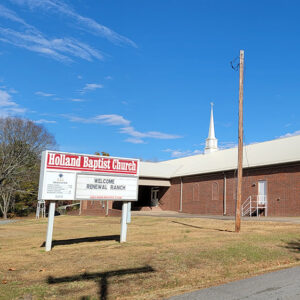 Red brick church building with steeple and sign "Holland Baptist Church"