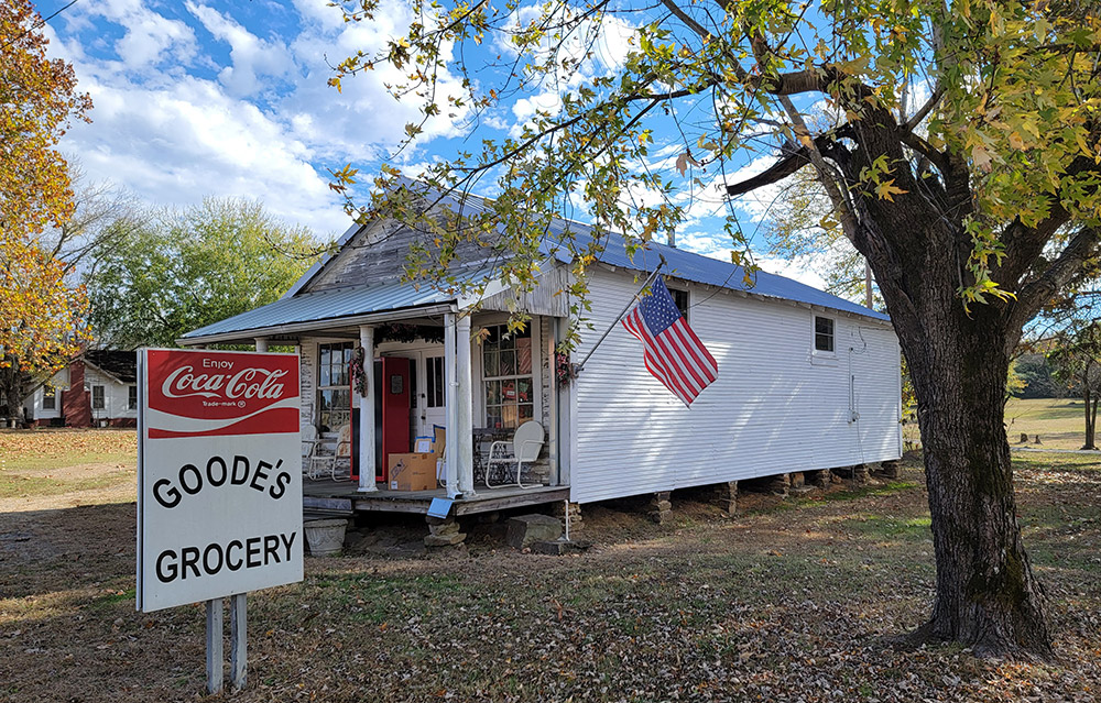 Single story white wooden grocery store building with covered entrance and sign "Goode's Grocery"