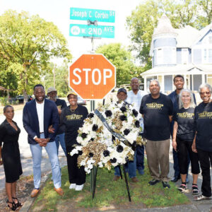 Group of African American men and women gathered around a wreath and a stop sign and street sign