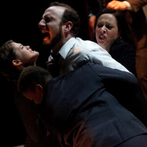 Male actor on stage screaming while three female actors hold on to him