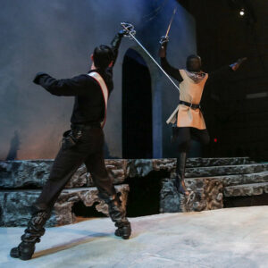 Two actors dressed mostly in black sword-fighting