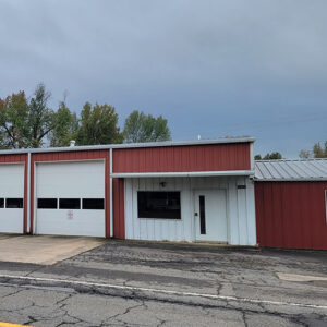 Single story red metal building with four white garage doors