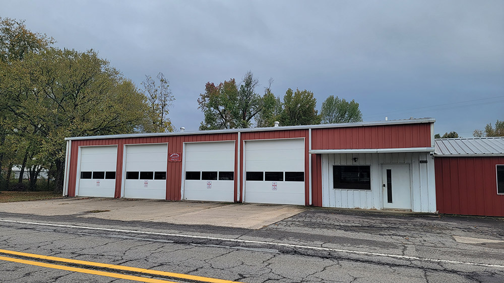 Single story red metal building with four white garage doors
