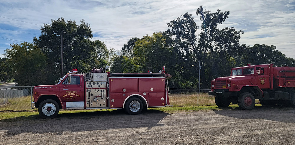 Red fire department vehicles parked on gravel road with trees in background