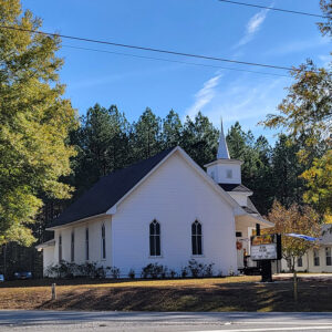 white wooden church building with small steeple and trees in background