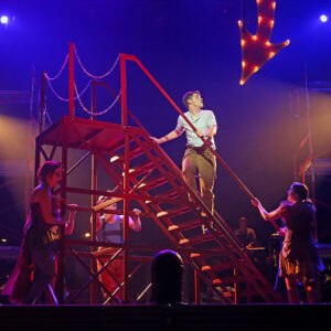 Actors on stage standing around and climbing a red staircase