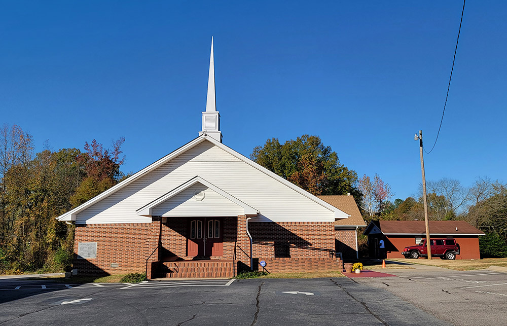 red brick church building with white steeple and parking lot