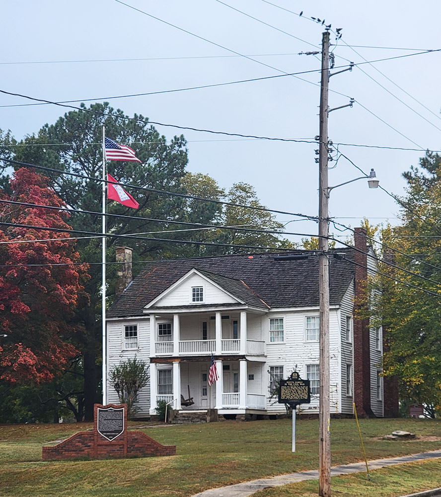 Multistory white wooden house with covered front porches on both levels and flagpoles in front