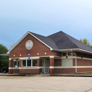 Single story red brick post office building with glass doors and windows in front and parking lot