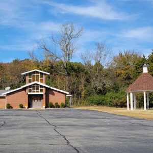 Orange brick church building with tower above entrance and parking lot and gazebo