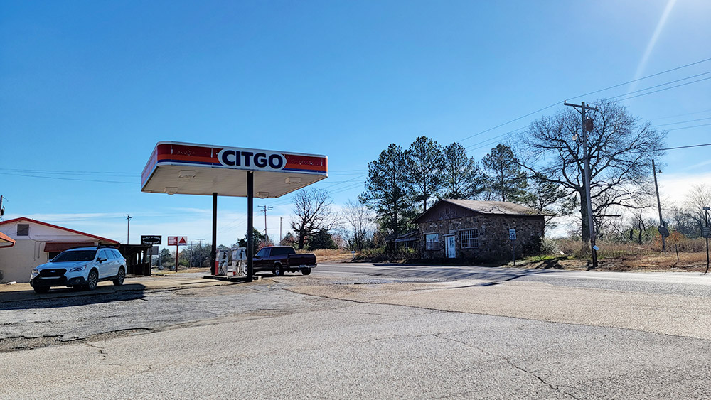 Small town street scene with gas station and abandoned stone house