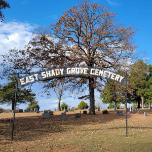 Cemetery with graves and trees and an arched sign saying "East Shady Grove Cemetery"