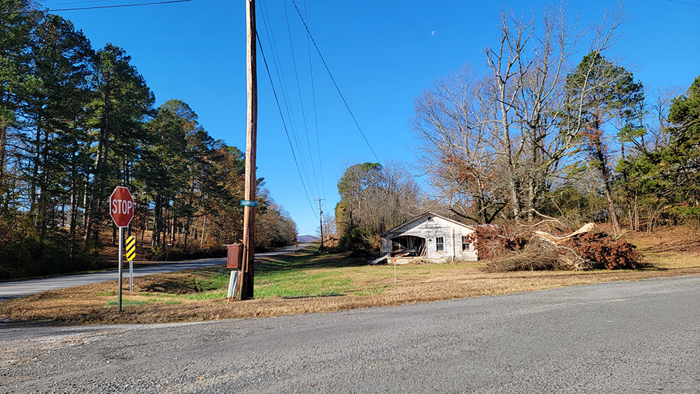 Intersection of two rural roads with abandoned house and brush pile