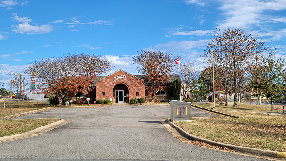 Multistory red brick library building with arched covered entrance and parking lot