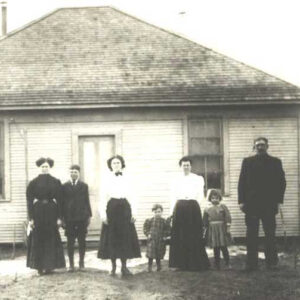 seven white people dressed in formal clothes standing in a row in front of a building