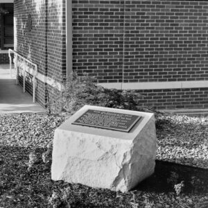 Concrete and brass memorial with a poem on it placed next to brick building