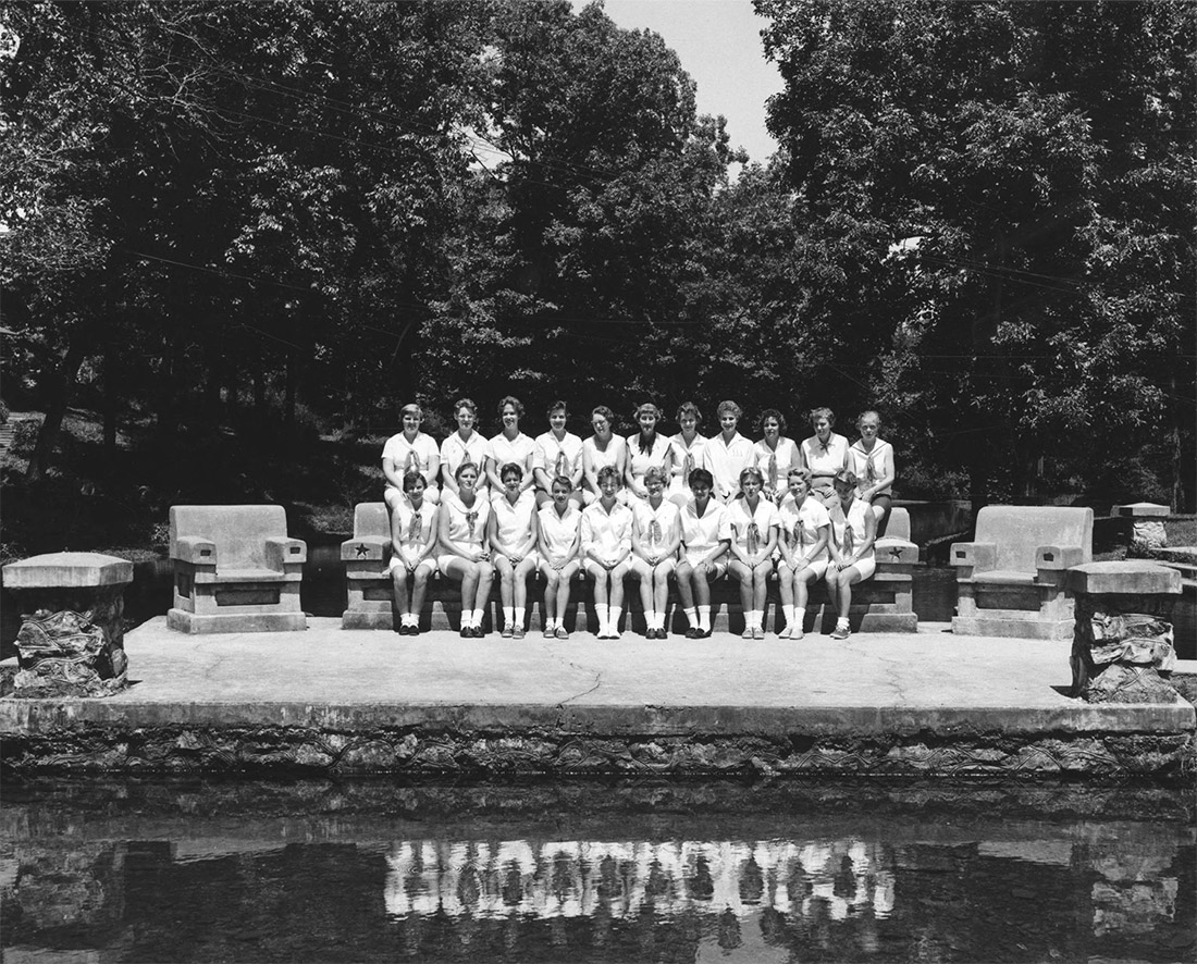Group of white women and girls dressed in white sitting on two levels of a large stone bench