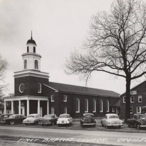 Cars parked in front of brick church building with tower and covered entrance