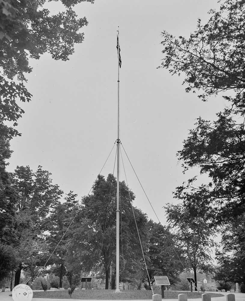Flagpole in a cemetery surrounded by trees