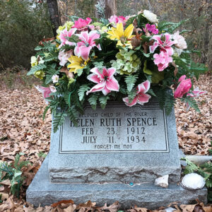 Tombstone in wooded area with flowers around it