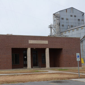 Single story red brick building with recessed entrance and columns beside silo