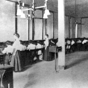 Large group of white women and one white man in a room with equipment and tables