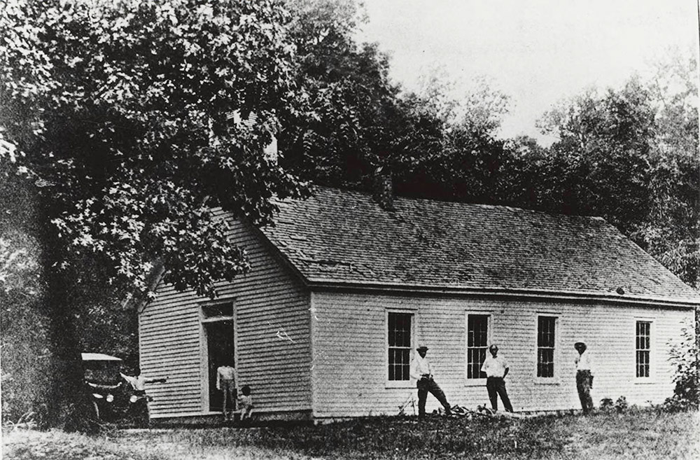 African American people standing around white wooden church building