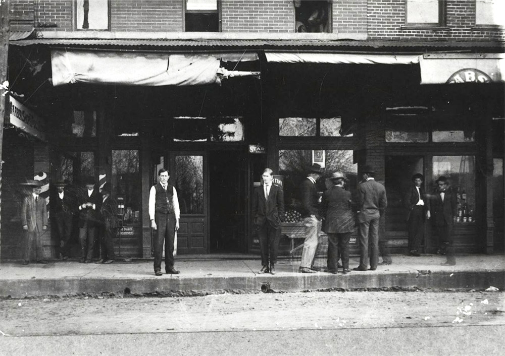 Group of white men standing on sidewalk in front of building